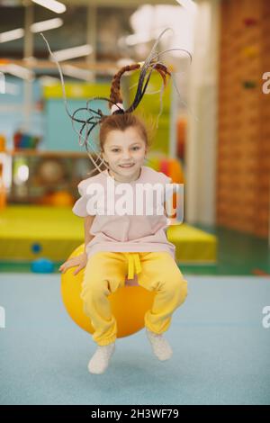 Les enfants font des exercices avec un grand ballon en salle de gym à la maternelle ou à l'école primaire. Concept de sport et de fitness pour enfants. Banque D'Images