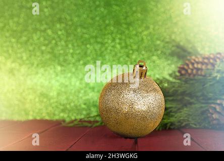 Boule dorée étincelante sur fond de bois rouge avec branches d'épinette verte avec des cônes.Arrière-plan vert flou.Noël, nouvel an.Station santé Copy Banque D'Images