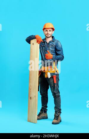 Portrait pleine longueur de jeune menuisier montrant les pouces vers le haut signe tenant pile de bois de bois et Banque D'Images