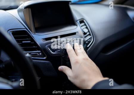 la main d'un homme atteint le tableau de bord de la voiture et appuie sur le bouton avec son doigt Banque D'Images