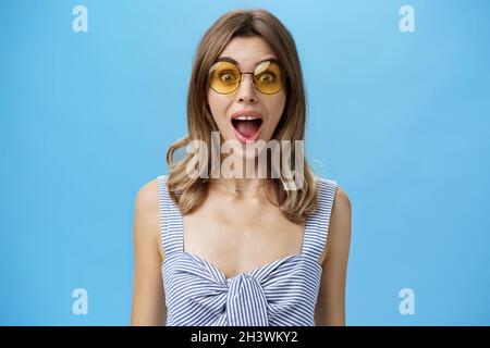 Prise de vue à la taille de la femme caucasienne excitée surprise et émotive charismatique dans les lunettes de soleil tendance ouvrant la bouche de l'étonnement et Banque D'Images