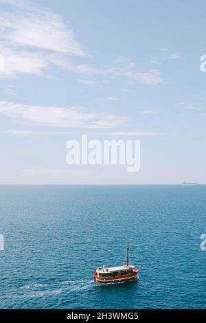 Un bateau rouge de plaisir navigue sur la mer sur le fond du ciel et de l'horizon. Beaucoup de place pour le texte. Banque D'Images