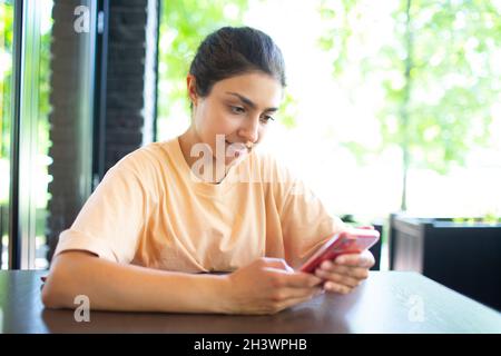 Bonne jeune femme indienne parlant sur un téléphone portable assis à l'extérieur café. Banque D'Images