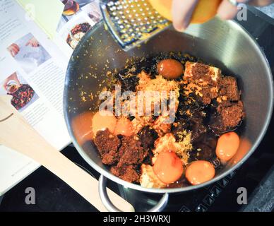 Ingrédients dans un bol à mélanger prêt à faire dans un gâteau de Noël.Le livre de recettes est en arrière-plan et le zeste est râpé dans le bol Banque D'Images