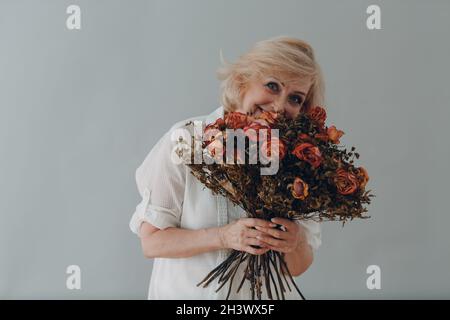 Positive souriante femme âgée tient dans les mains rose fleurs bouquet. Banque D'Images