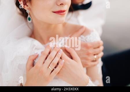 Le marié épouse doucement la mariée de derrière sur leurs mains sont des anneaux de mariage Banque D'Images