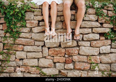 Jambes d'un homme et d'une femme assis côte à côte côté de la clôture en pierre Banque D'Images