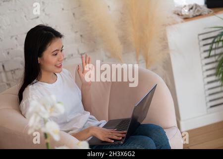 Portrait d'une femme asiatique appréciant l'utilisation d'un ordinateur portable à l'intérieur de l'appartement salon intérieur.Concept de flux de webinars par appel vidéo. Banque D'Images