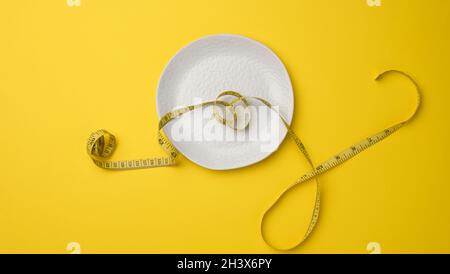 Vider la plaque en céramique blanche et le ruban de mesure sur fond jaune.Concept de nutrition saine Banque D'Images