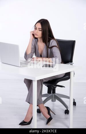 Femme d'affaires à son bureau.Elle a de longs cheveux noirs et porte une combinaison grise.Elle est sérieuse et regarde son ordinateur portable. Banque D'Images