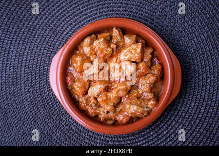 Assiette en argile remplie de viande avec de la tomate et isolée, sur une nappe sombre. Banque D'Images