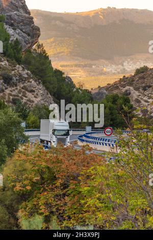 Camion avec semi-remorque réfrigérée roulant sur une autoroute entre les montagnes et bordé d'arbres en automne. Banque D'Images