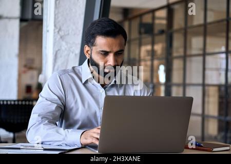 Homme d'affaires hispanique ethnique concentré travaillant dans le bureau à l'aide d'un ordinateur portable. Banque D'Images