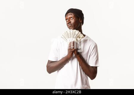 Portrait d'un homme chanceux afro-américain rêveur et réfléchi, tenant de l'argent et de la pensée, fond blanc Banque D'Images