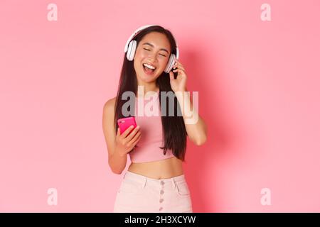 Portrait à la taille haute d'une jolie fille asiatique proche des yeux et chantant le long d'une chanson tout en écoutant de la musique dans un casque ou un lecteur Banque D'Images