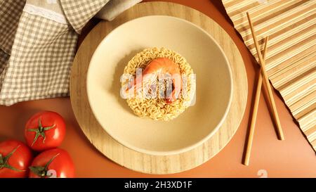 Soupe épicée de nouilles instantanées avec crevettes et légumes. Soupe de crevettes, cuisson, nourriture.Vermicelles en forme de cercle séchées dans une assiette. Banque D'Images