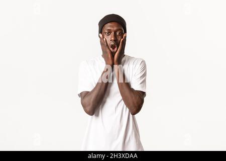 Portrait d'un gars cool afro-américain choqué et impressionné dans le bonnet, la mâchoire de chute et le souffle demandé, regarder la caméra sur blanc Banque D'Images