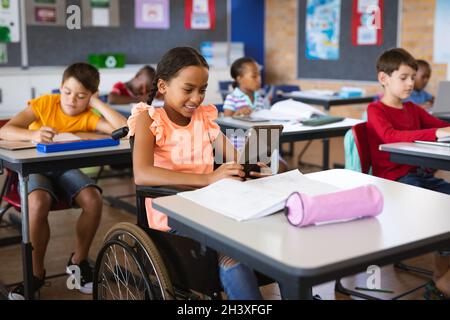 Fille afro-américaine handicapée utilisant une tablette numérique tout en étant assise sur un fauteuil roulant à l'école primaire Banque D'Images