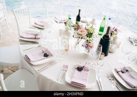 Réception de table de dîner de mariage.Assiettes carrées blanches sur une table ronde avec serviettes de table en chiffon rose et coeur noir.Chaises blanches Chia Banque D'Images