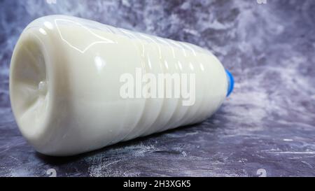 Une bouteille en plastique avec un bouchon bleu de lait régulier frais sur fond en marbre gris foncé ou en béton.Vue de face rapprochée.Monde Banque D'Images