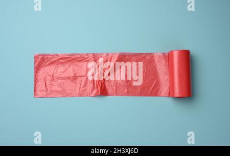 Rouleau de sacs en plastique transparent rouge pour poubelle sur fond bleu Banque D'Images