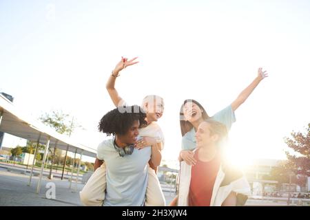 Deux jeunes hommes qui offrent à leurs amies des promenades en pigeyback dans la ville.Des amis joyeux qui apprécient l'amitié et les succès en plein air. Banque D'Images