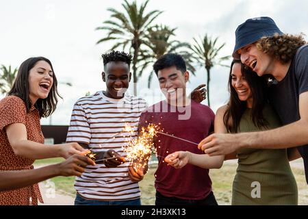 Des gens multiraciaux heureux qui rient et s'amusent ensemble avec des gens qui font des étincelles en plein air Banque D'Images