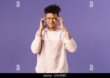 Portrait d'intense, pressé jeune étudiant de sexe masculin surtravaillé, se sentir fatigué et étourdi, grimacing de sensation douloureuse dans la tête, ayant Banque D'Images