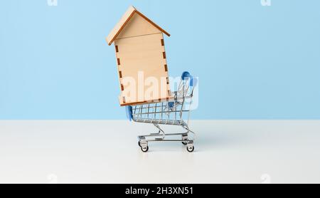 Maison en bois dans un chariot miniature en métal sur fond bleu.Concept d'achat immobilier, hypothèque Banque D'Images