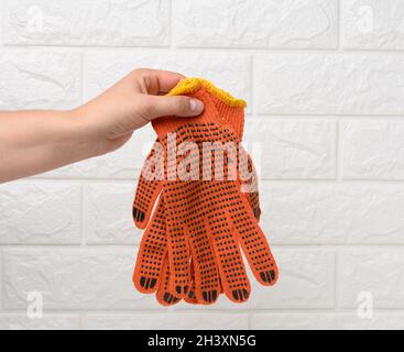 La main femelle tient des gants de travail en tissu orange sur un fond blanc Banque D'Images