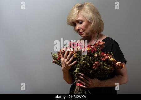 La femme âgée contrariée tient avec un vieux bouquet de fleurs de rose sec. Banque D'Images