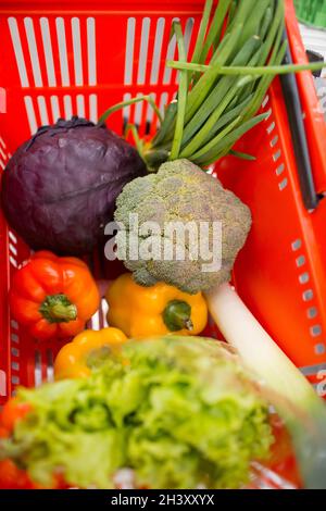 Panier rouge avec légumes et herbes dans le magasin. Poivre, brocoli, oignon, salade, tomates, chou Banque D'Images