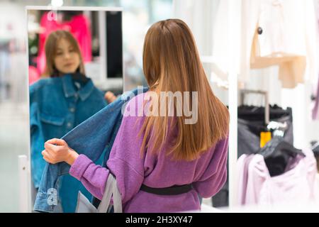 La jeune femme choisit et essaie de regarder des vêtements de miroir dans la boutique Banque D'Images