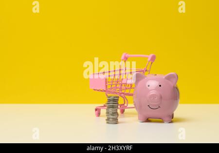 Banc de piggy en céramique rose et une pile de pièces de monnaie sur une table blanche, fond jaune.Concept d'épargne, planification budgétaire Banque D'Images