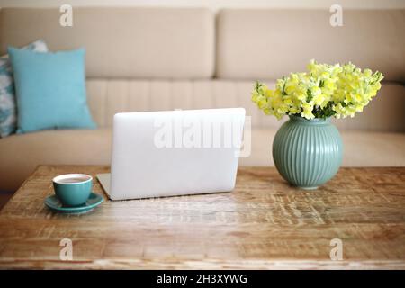 Ordinateur portable ouvert, tasse de café et vase avec fleurs jaunes sur table en bois rétro texturé dans la salle de séjour Banque D'Images