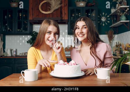 Des femmes heureux amis à la maison assis et souriant avec blanc gâteau d'anniversaire Banque D'Images