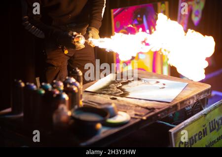 Un jeune artiste de rue finissant ses œuvres d'art avec de la peinture de couleur vaporisée et du feu dans la nuit sombre Banque D'Images