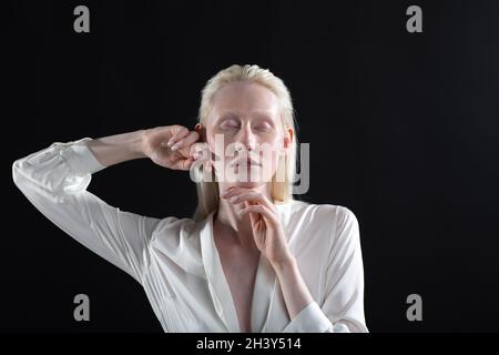 Jeune femme blonde albino faisant la gymnastique faciale automassage et des exercices rajeunissants sur fond noir Banque D'Images