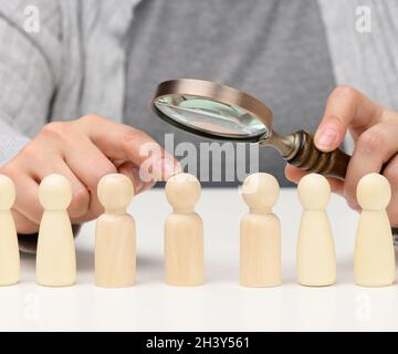 Figurines d'hommes sur une table blanche, une main femelle tient une loupe sur une. Concept de recherche d'employés dans la co Banque D'Images