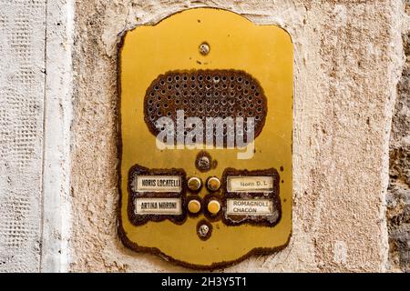 Venise, Italie - 25 juillet 2020 : interphone jaune antique pour quatre appartements avec noms d'abonnés sur un mur en pierre. Banque D'Images