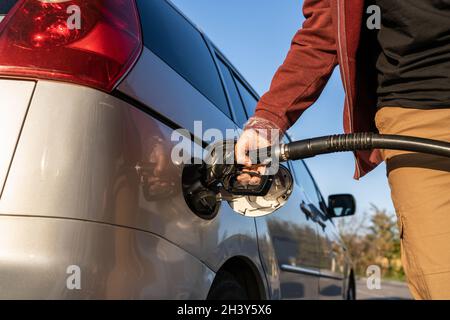 Gros plan sur la main d'un homme caucasien inconnu tenir la buse de pompe à gaz noire versant de l'essence dans le réservoir de carburant ravitaillant du pétrole vers le véhicule en auto-service Banque D'Images