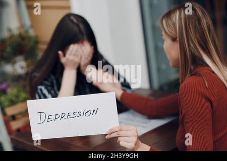 Concept de dépression cachée.Femme pleure.Deuxième femme tenant un papier blanc étiqueté de dépression dans la main.Deux femmes talki Banque D'Images