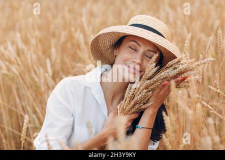 Jeune femme en chapeau de paille tenant une feuille d'épis de blé au champ agricole Banque D'Images