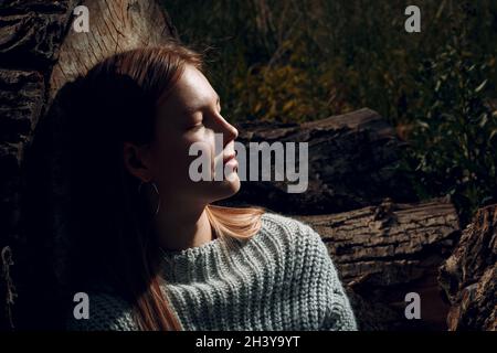 Jolie jeune femme rétro-éclairée à scier l'arbre à l'extérieur dans le parc en été. Banque D'Images