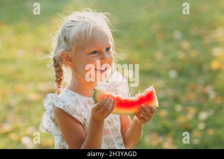 Jolie petite fille blonde avec pastèque sur l'herbe stationnement Banque D'Images