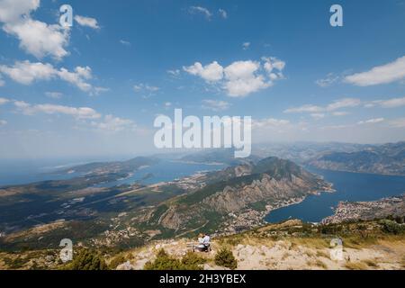 Un homme et une femme sont assis dans une étreinte sur un banc, une vue panoramique de la baie de Kotor s'ouvre devant eux Banque D'Images