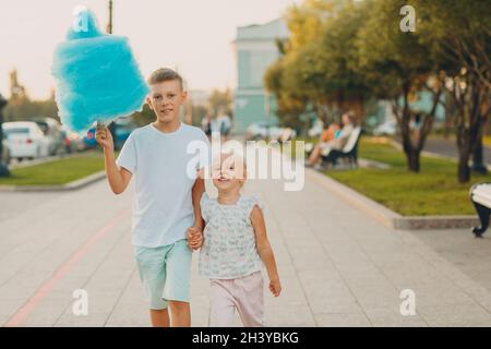 Les enfants heureux garçon et fille mangeant des bonbons en coton bleu à l'extérieur Banque D'Images