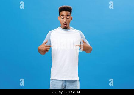 Impressionnez l'homme afro-américain émotif avec la barbe et la coiffure afro lèvres pliantes dans le son wow pointant vers la poitrine ou le centre avec Banque D'Images