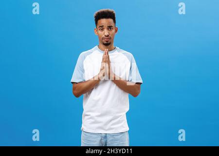 Aidez-moi à vous supplier.Charmant petit ami afro-américain mignon et charmant avec une coupe de cheveux bouclés et une barbe qui tient les mains Banque D'Images