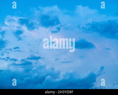 Un cadre plein de ciel surréaliste avec de beaux nuages colorés de bleu, blanc gris et une touche de rose pastel, rétroéclairé de la lumière du soleil Banque D'Images